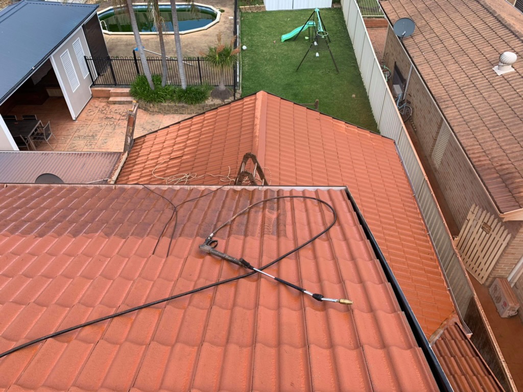 Terracotta tiled roof part-way through a high-pressure clean, before repainting