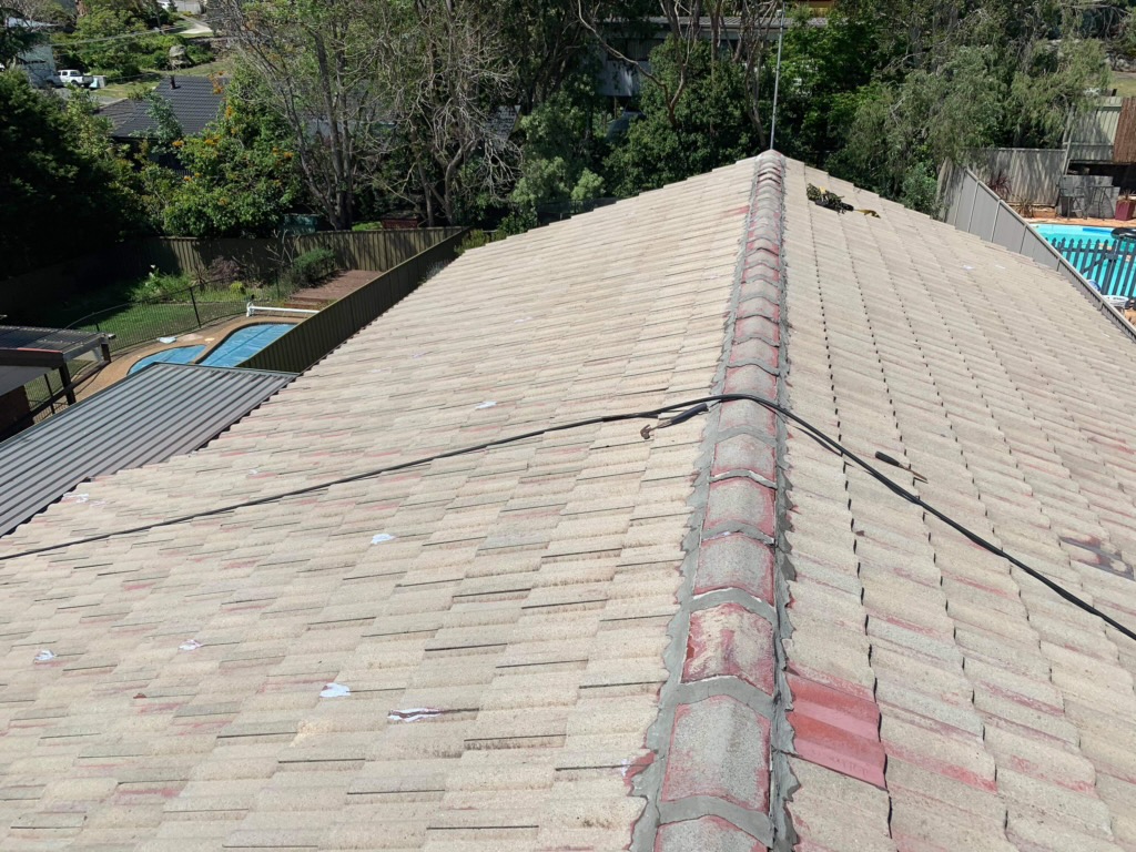 Worn roof tiles with faded colour and deteriorated ridge pointing before restoration