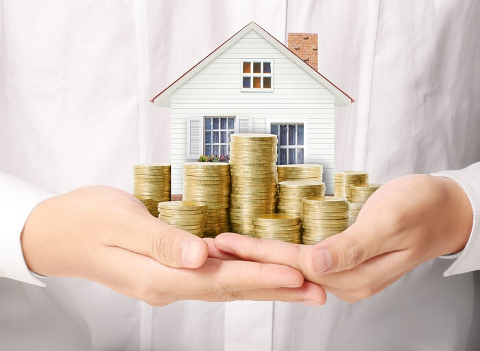 Hands holding a model house and varying stacks of coins