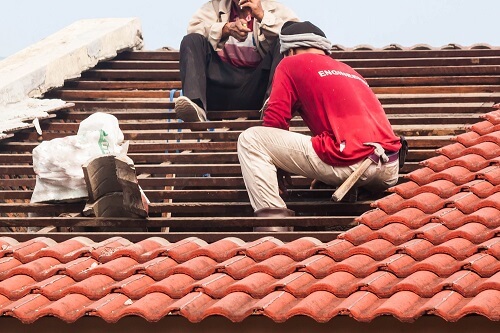 Workers replacing clay tiles on a roof